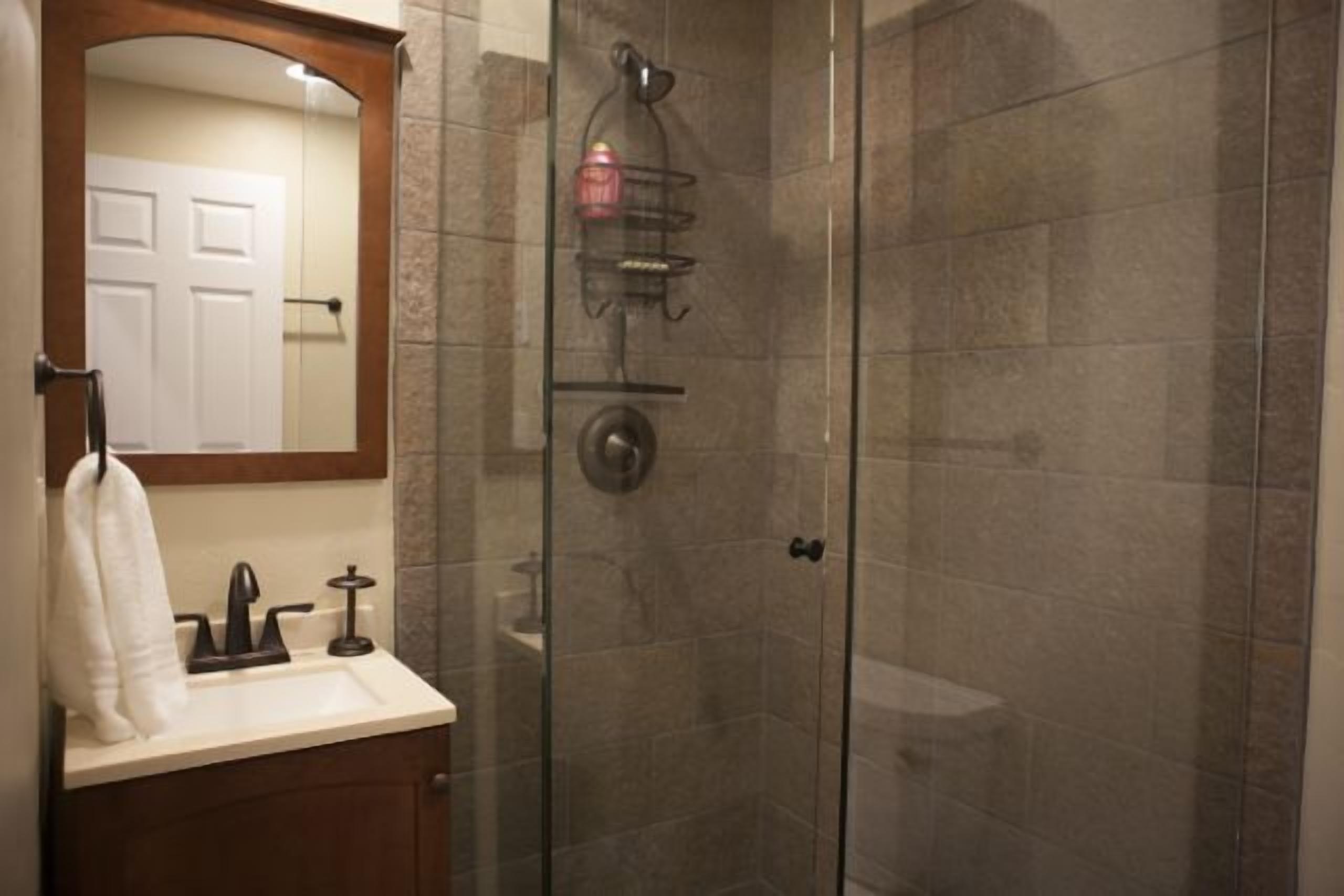Une salle de bain avec une douche à parois de verre, un lavabo avec un miroir au-dessus et une serviette accrochée au mur.