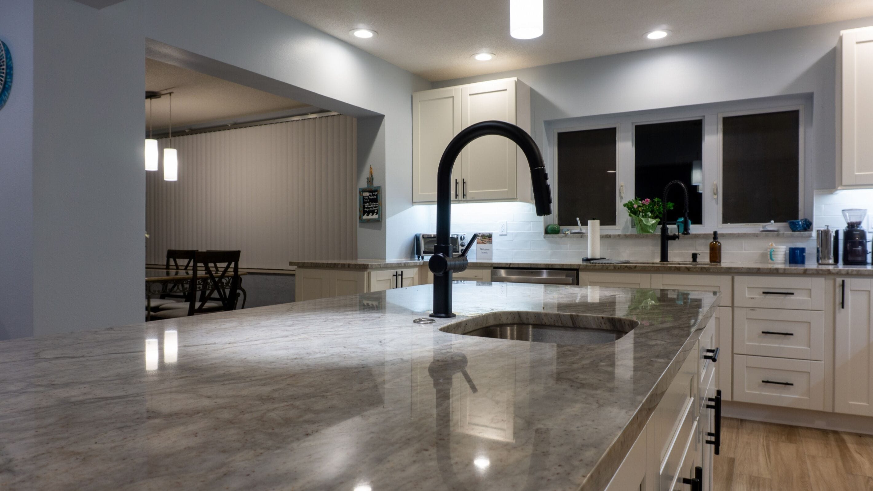 A modern kitchen with a large island, white cabinetry, and a black faucet.
