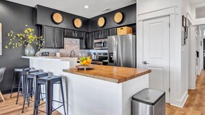 A modern kitchen with dark cabinets, a wooden island, stainless steel appliances, and a vase of yellow flowers. - Palms A1: Best Prices to Be Ground Level Directly  on the Beach  (Santa Rosa Beach)