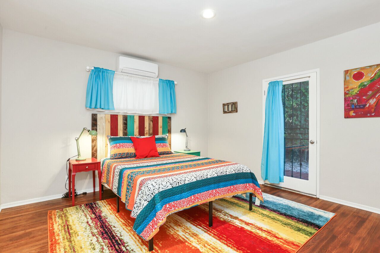 Une chambre à coucher avec un lit, une table de chevet, une lampe, une fenêtre avec des rideaux et une porte.