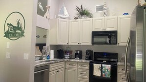 A kitchen with white cabinets, a stainless steel refrigerator, a microwave, and an oven. There is a welcome sign on the wall and a small sailboat decoration. - Super Clean and Super Comfortable with boat ramp under half mile down the road. (Crystal River)