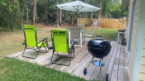 A backyard with a wooden deck, two green lawn chairs, a table, a barbecue grill, and a striped umbrella. - Super Clean and Super Comfortable with boat ramp under half mile down the road. (Crystal River)