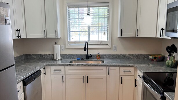 A kitchen with white cabinets, a stainless steel refrigerator, a dishwasher, a sink with a faucet, a microwave, and an oven.