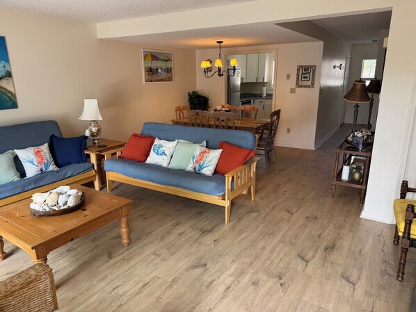 A living room with a blue sofa, wooden coffee table, and a dining area with a wooden table and chairs.