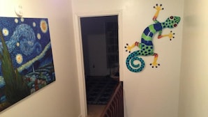 A hallway with a painting of a night scene on the left and a colorful frog decoration on the right.