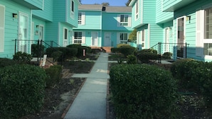 A row of turquoise buildings with a central pathway, surrounded by greenery.