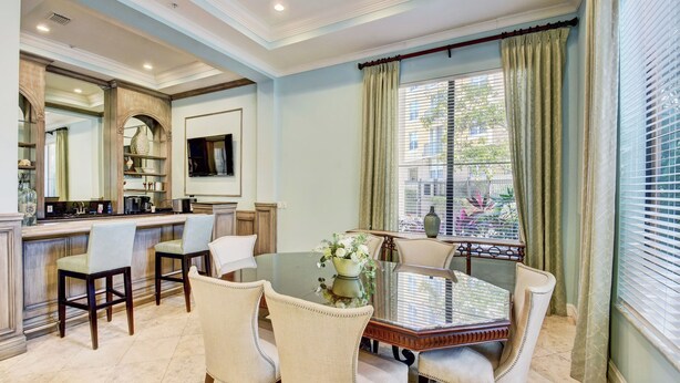Un comedor con mesa de vidrio, sillas tapizadas en beige y un florero decorativo con flores.