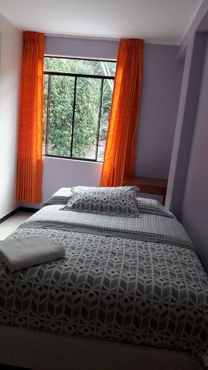 Un dormitorio con cama, cortinas naranjas y ventana con vista a follaje.