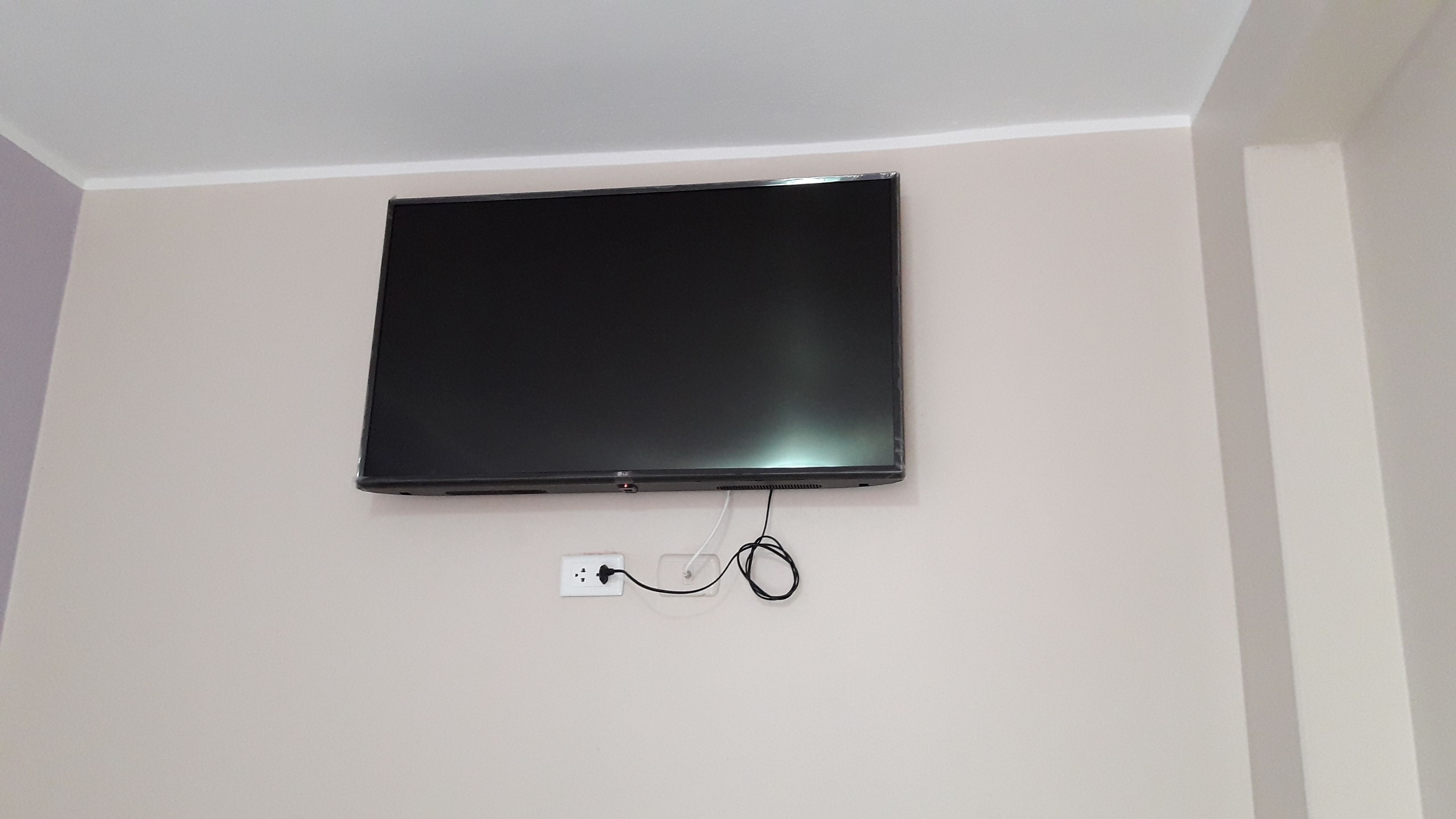 Un televisor de pantalla plana montado en una pared blanca, con un enchufe debajo.