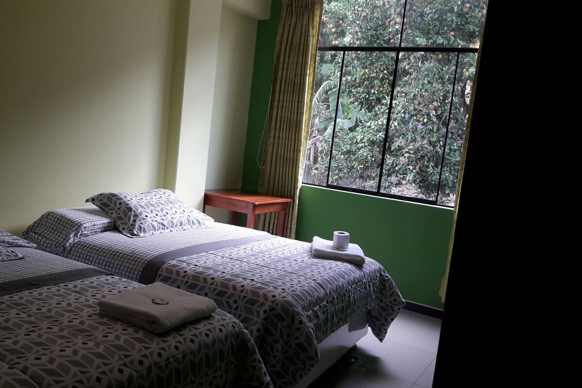 Una habitación con dos camas, una mesita y un ventanal con vistas a zonas verdes.