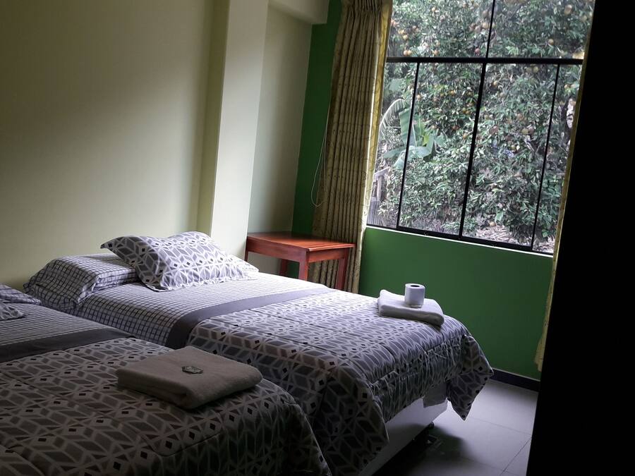 Una habitación con dos camas, una mesita y un ventanal con vistas a zonas verdes.