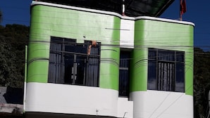 Un edificio de dos pisos con fachada verde y blanca, ventanas grandes y un porche cubierto.