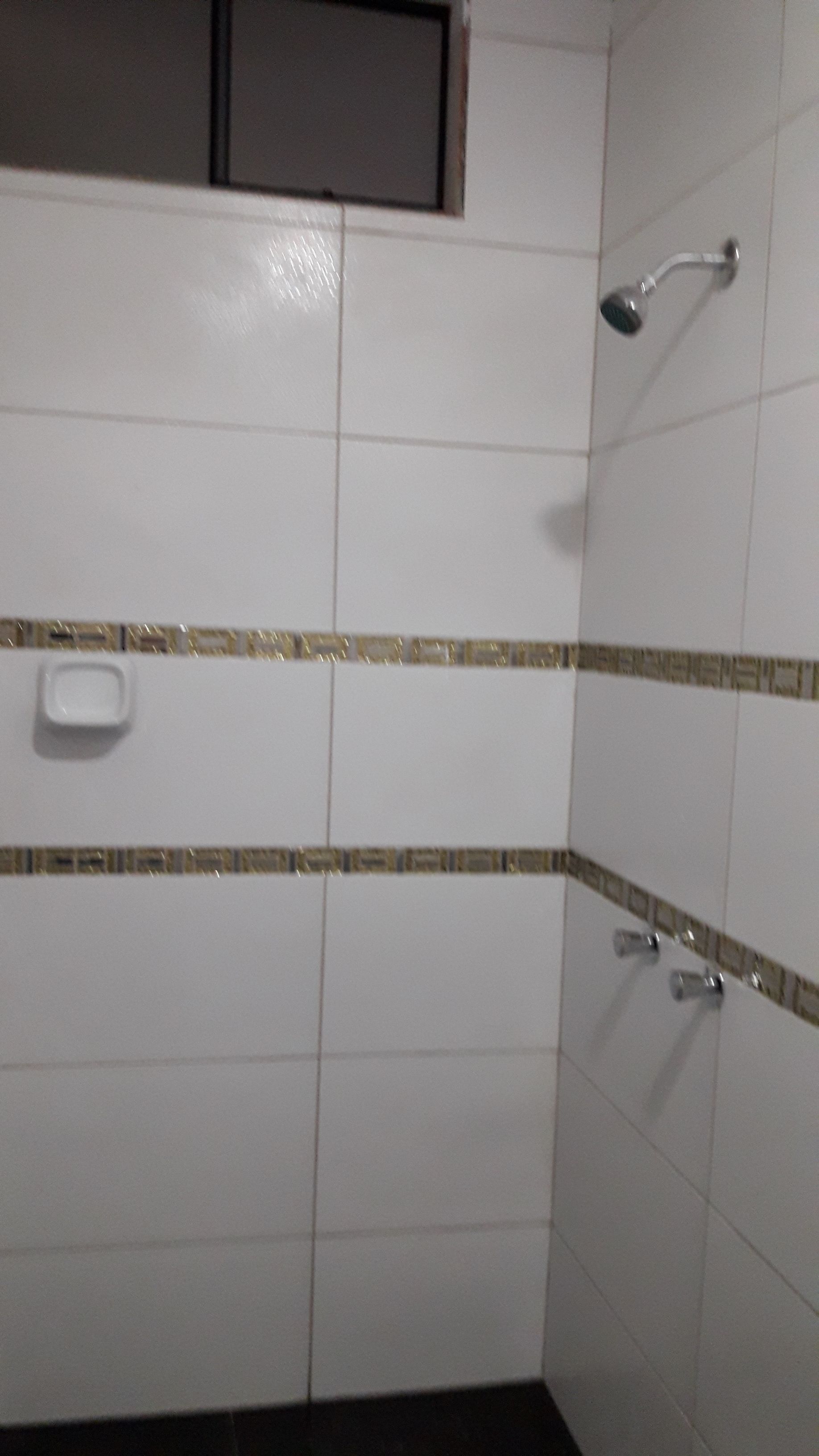 A bathroom with white tiles, a shower, and a small window.
