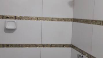 A bathroom with white tiles, a shower, and a small window.