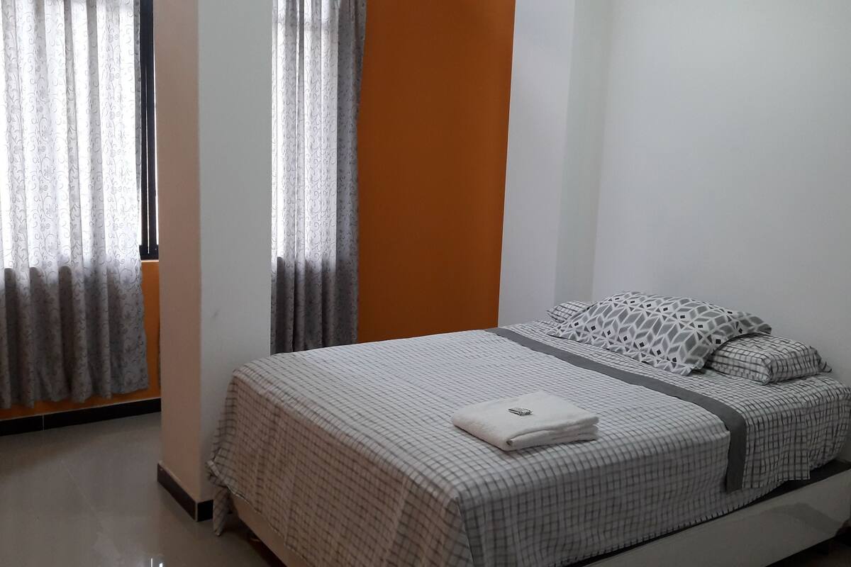 Un dormitorio con cama, cortinas y una pared lisa.