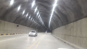 Un túnel con un solo auto circulando, paredes de concreto e iluminación en el techo.