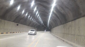 Un túnel con un solo auto circulando, paredes de concreto e iluminación en el techo.