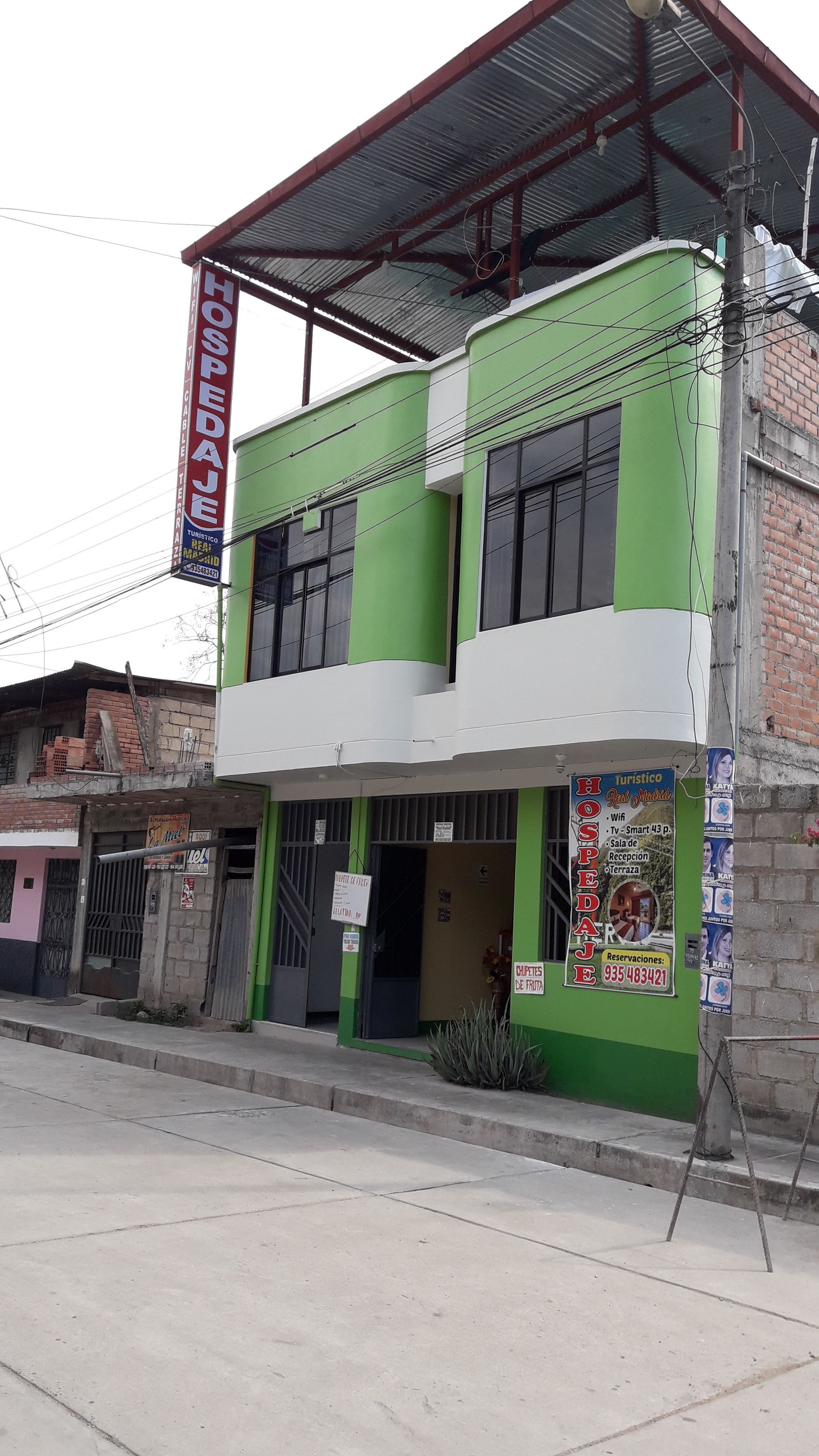 Un edificio de dos plantas con fachada verde y blanca, un vestíbulo cubierto y un letrero que anuncia un restaurante.