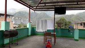 Un espacio exterior cubierto con vistas a montañas, una parrilla, una silla y ropa tendida en un tendedero.