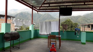 Un espacio exterior cubierto con vistas a montañas, una parrilla, una silla y ropa tendida en un tendedero.