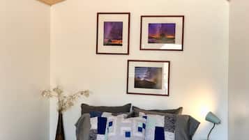 Um quarto com teto de madeira, uma cama com colcha, três quadros na parede, um vaso com flores e um abajur.
