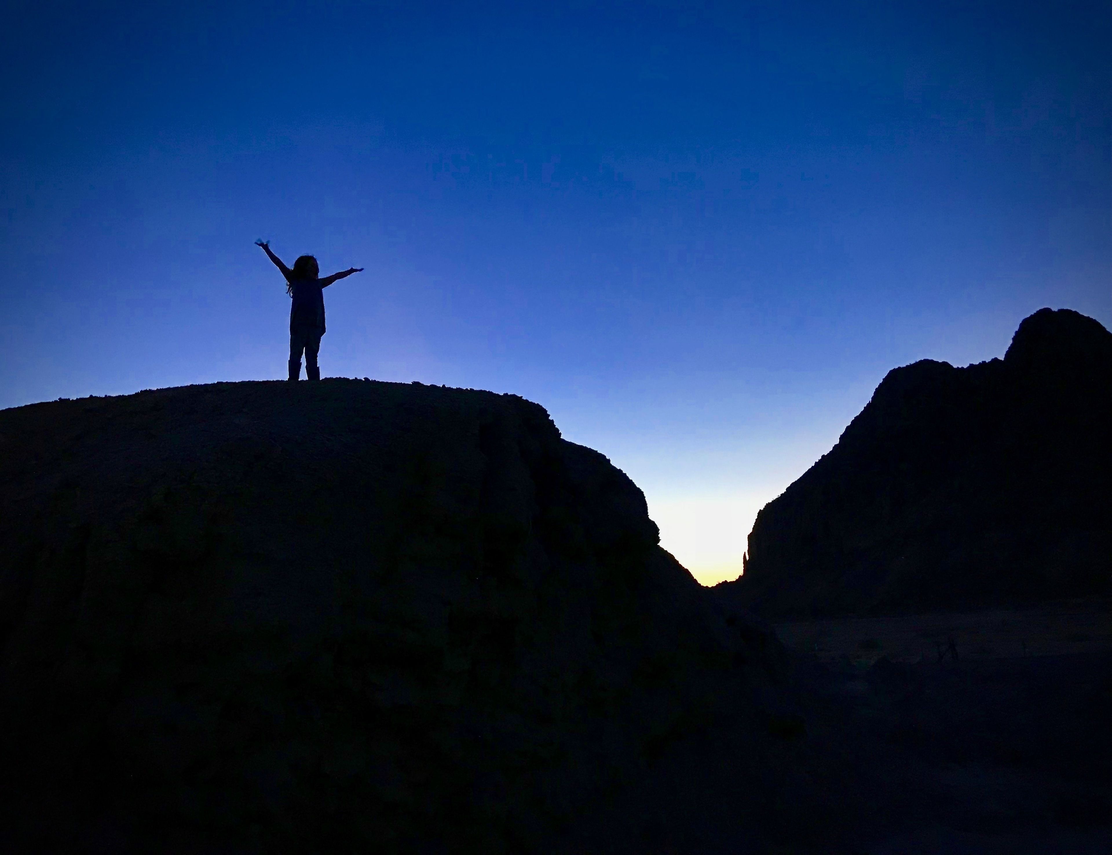 A silhouette of a person standing on a hill with arms raised, overlooking a valley.