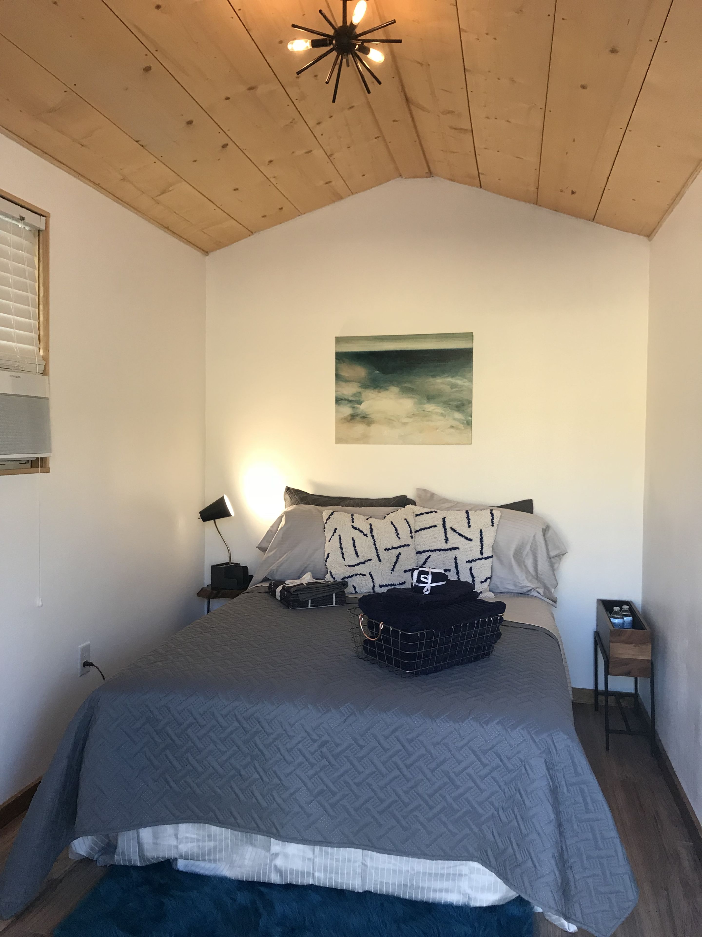 Un dormitorio con cama, un cuadro, una lámpara y una mesita.