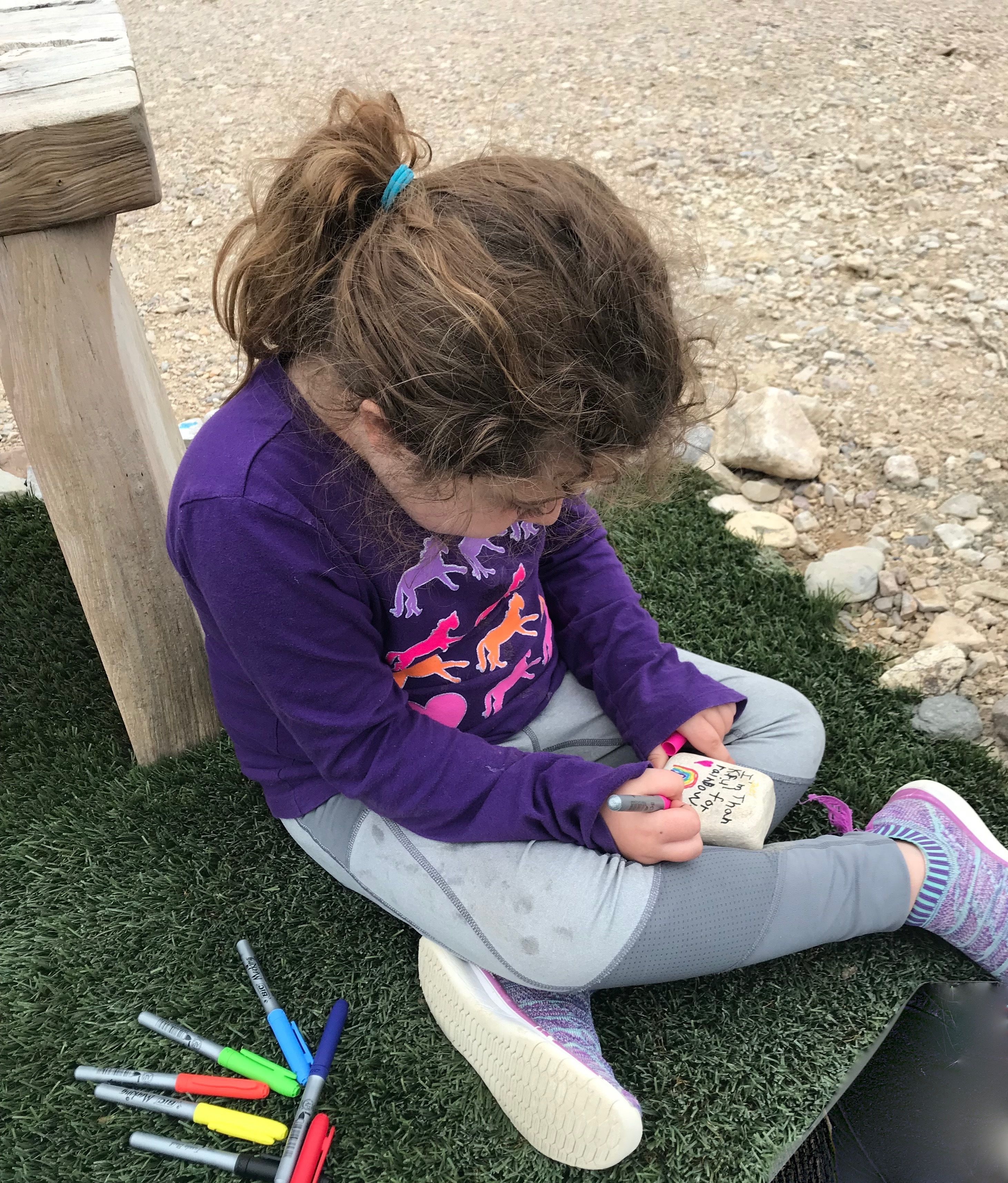 Un niño sentado sobre la hierba cerca de un banco de madera, sosteniendo un objeto pequeño.