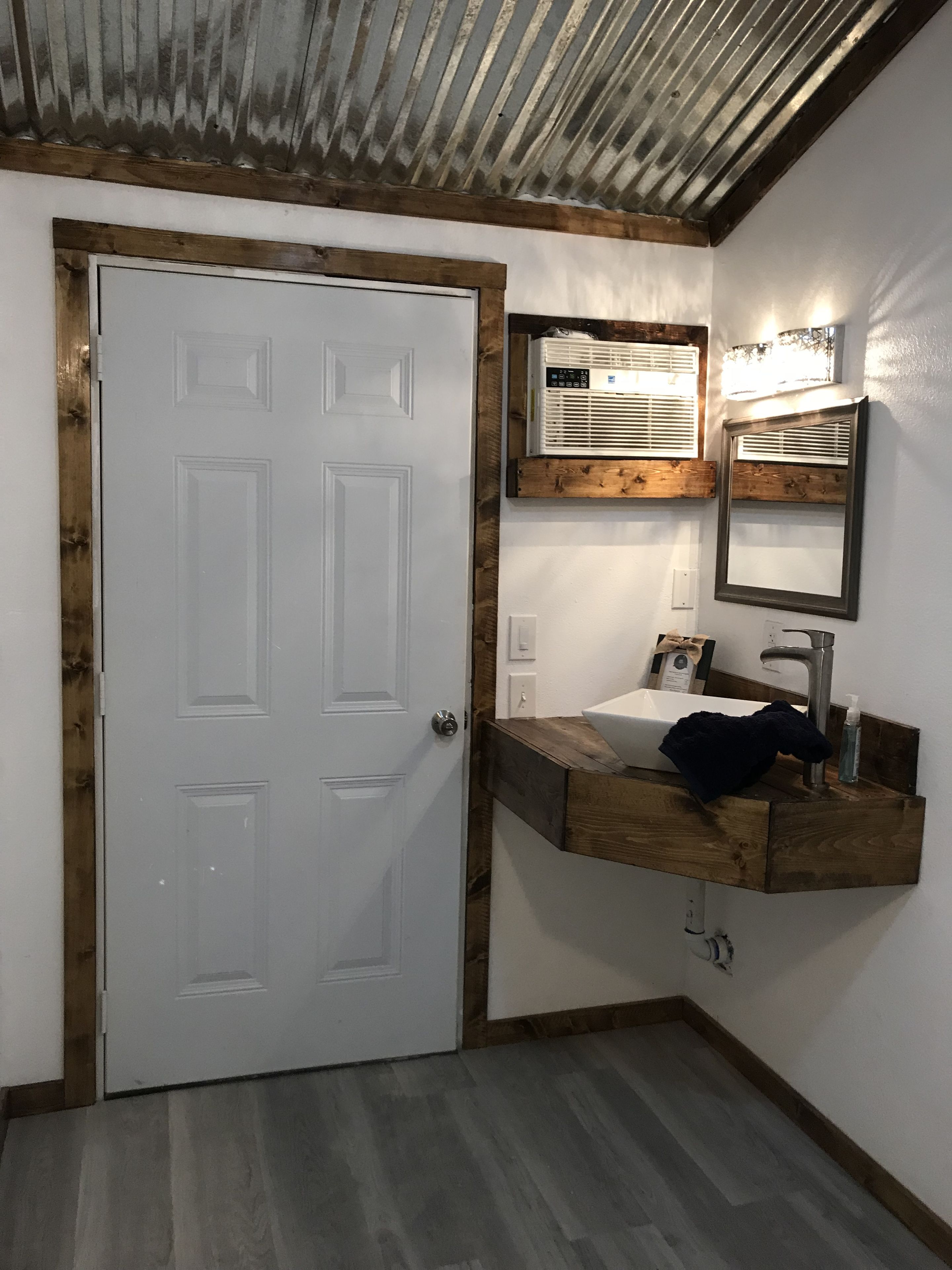 A bathroom with a white door, wooden vanity, and a mirror.
