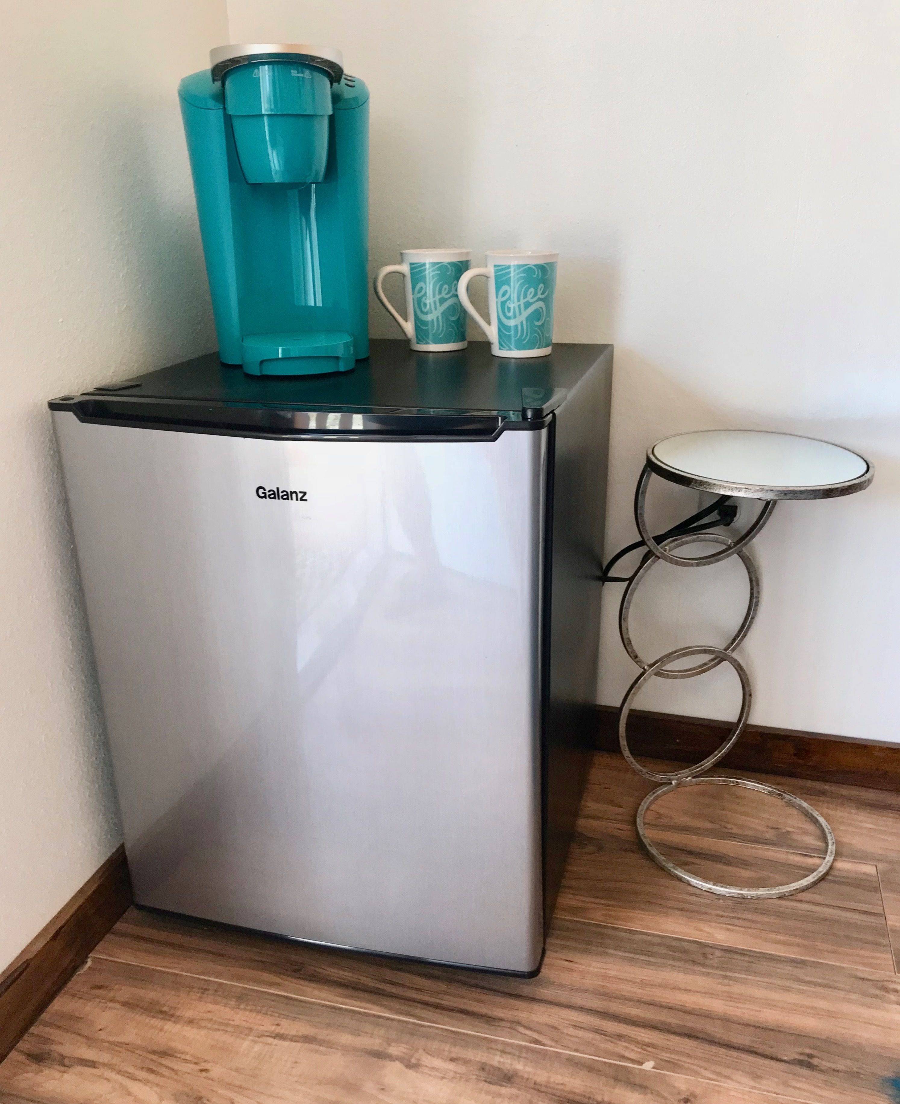 Una kitchenette compacta con un refrigerador Galanz, una cafetera color turquesa y dos tazas a juego.