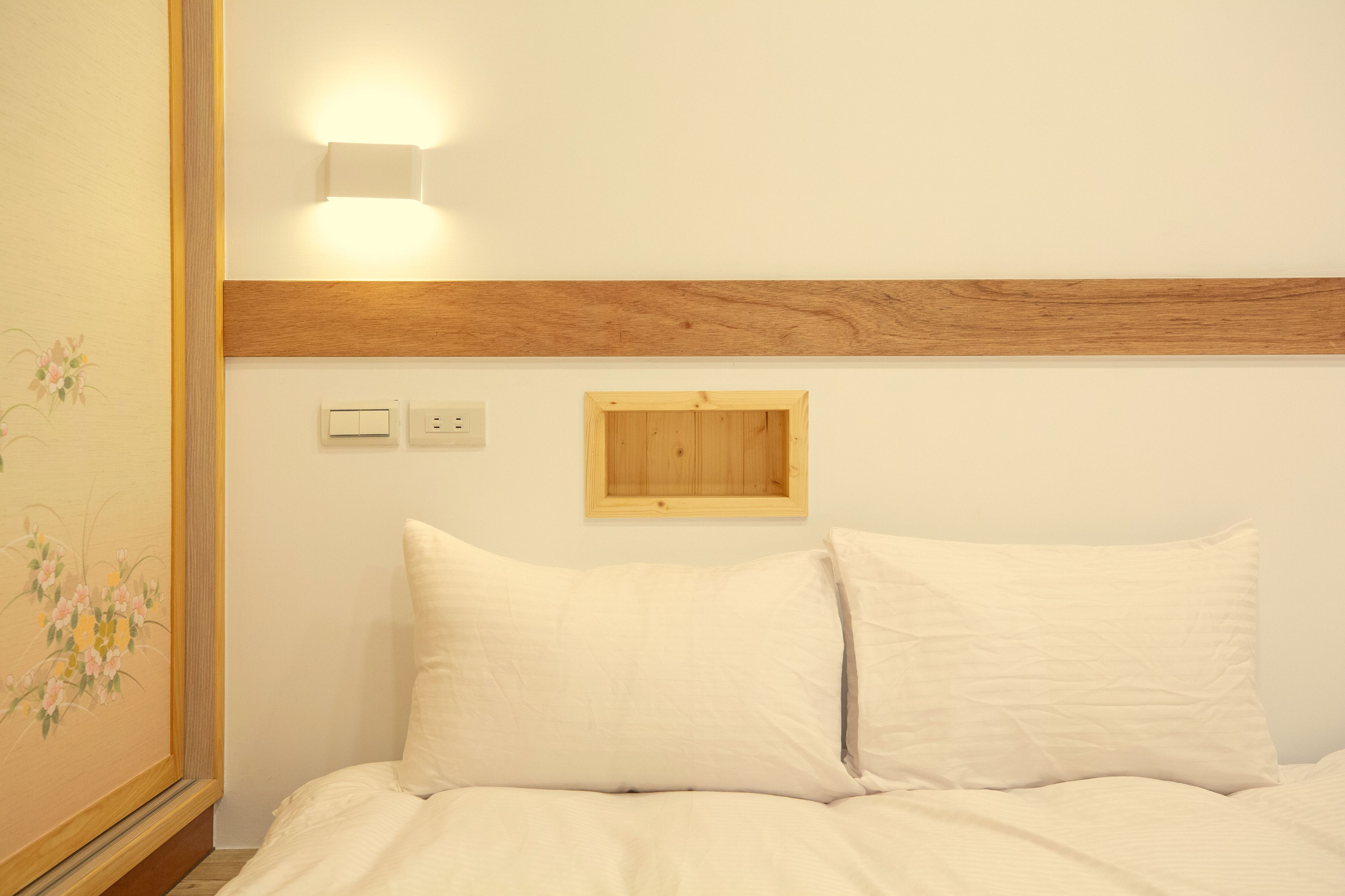 A bedroom with a wooden headboard, a wall-mounted light, and a small wooden panel above the bed.