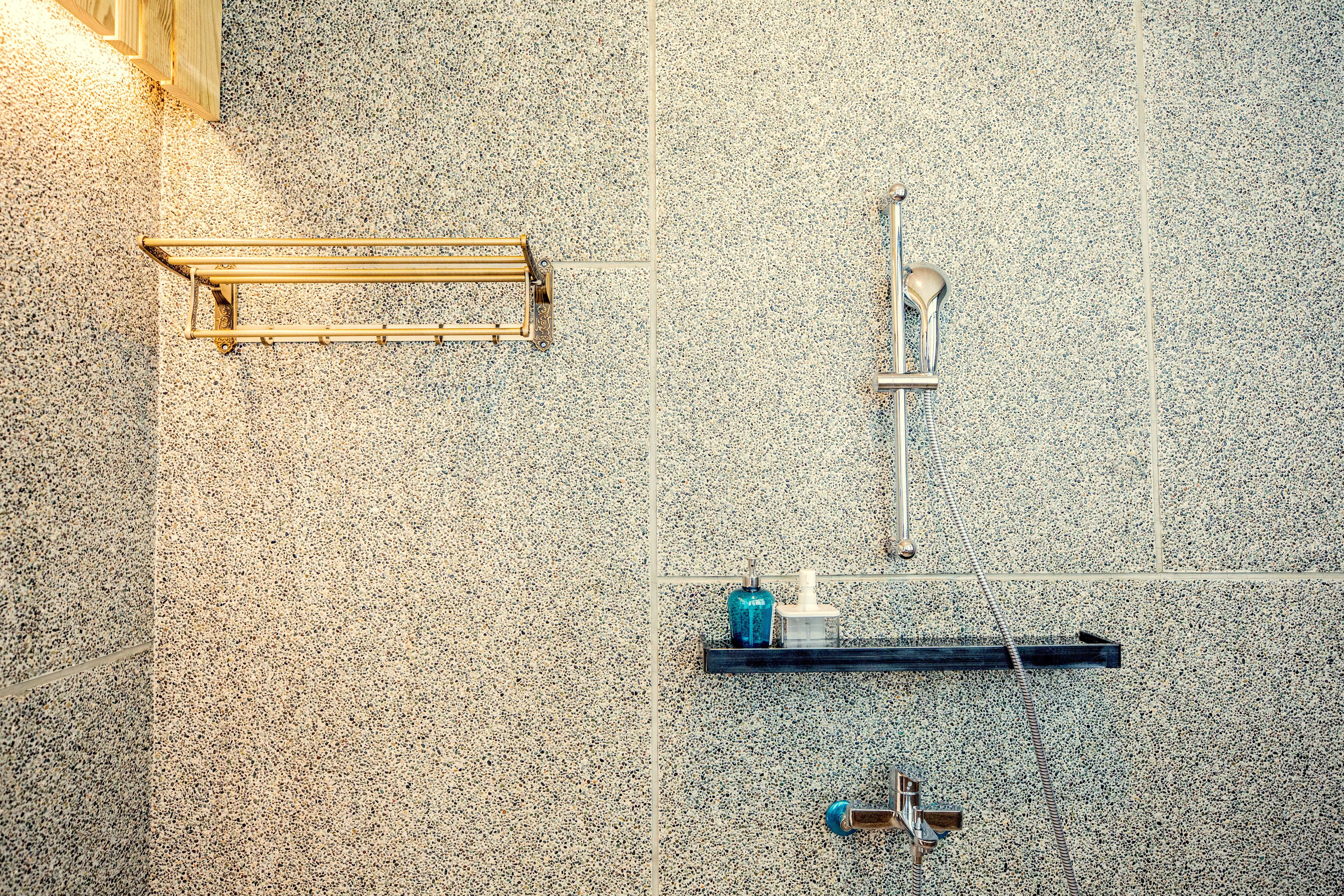 A bathroom with a granite wall, a towel rack, a showerhead, and a soap dispenser.