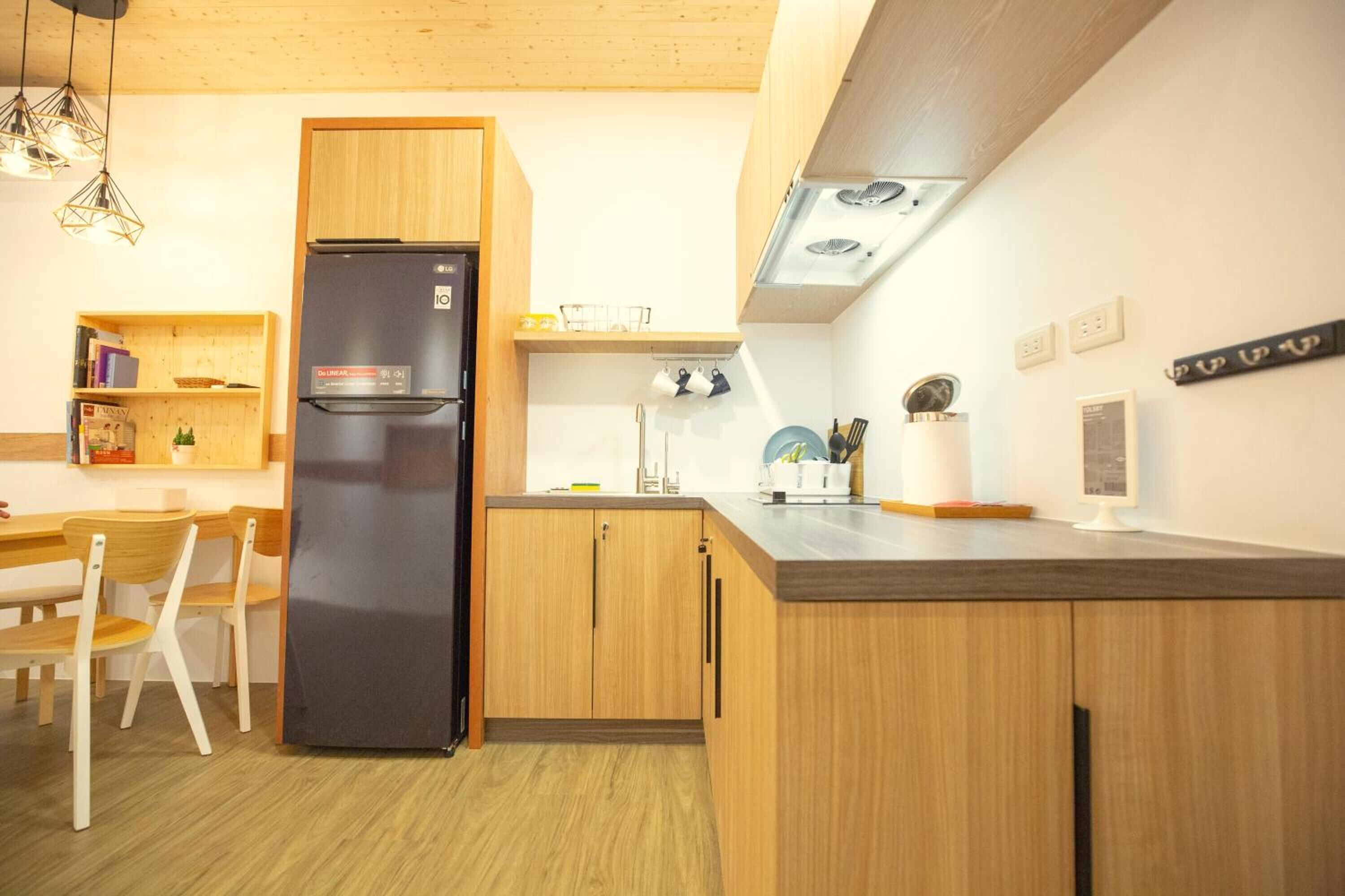 Une cuisine compacte avec des meubles en bois, un réfrigérateur noir, une table à manger avec des chaises et des luminaires suspendus.