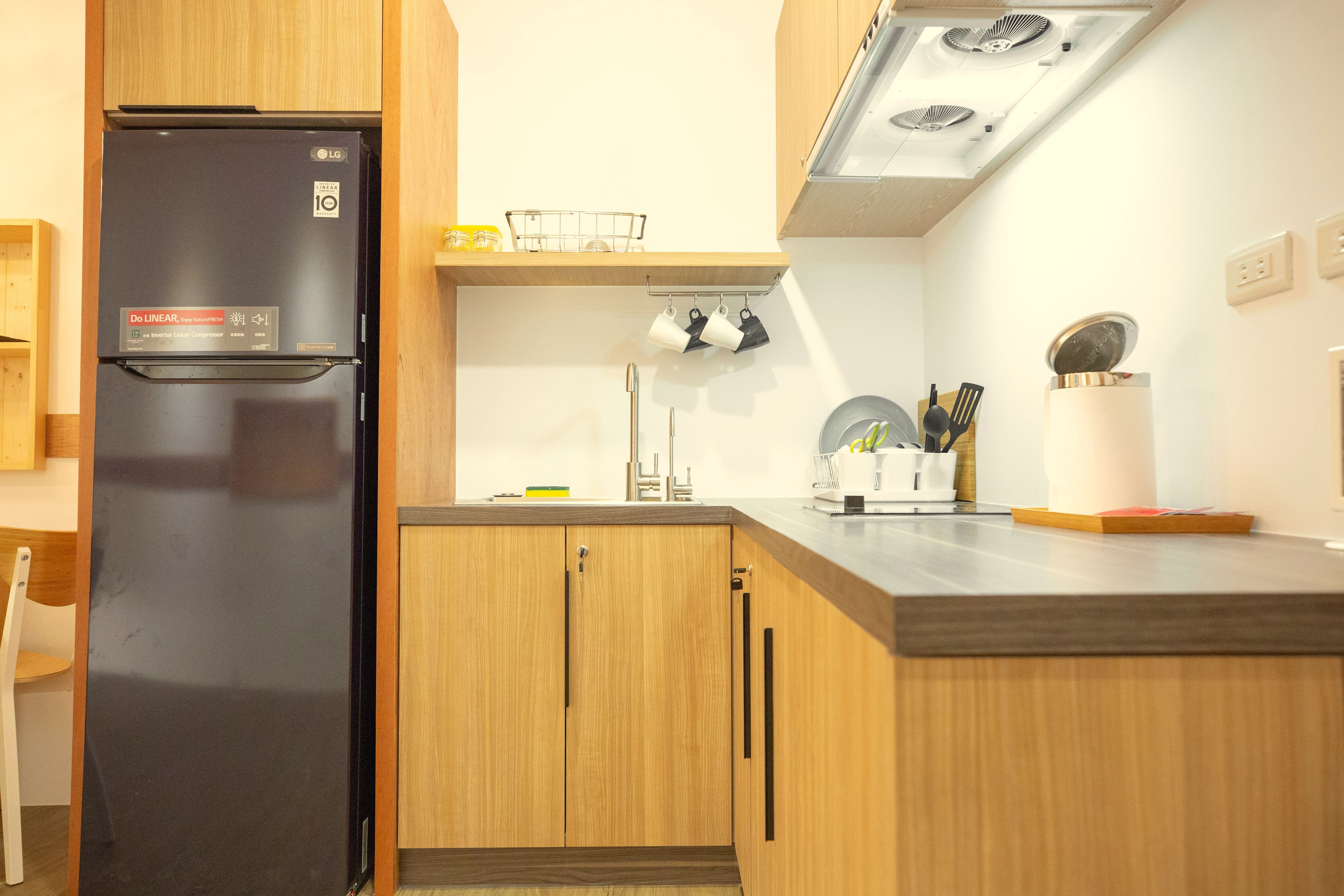 Una cocina moderna con armarios de madera, un refrigerador negro y un lavamanos de acero inoxidable.