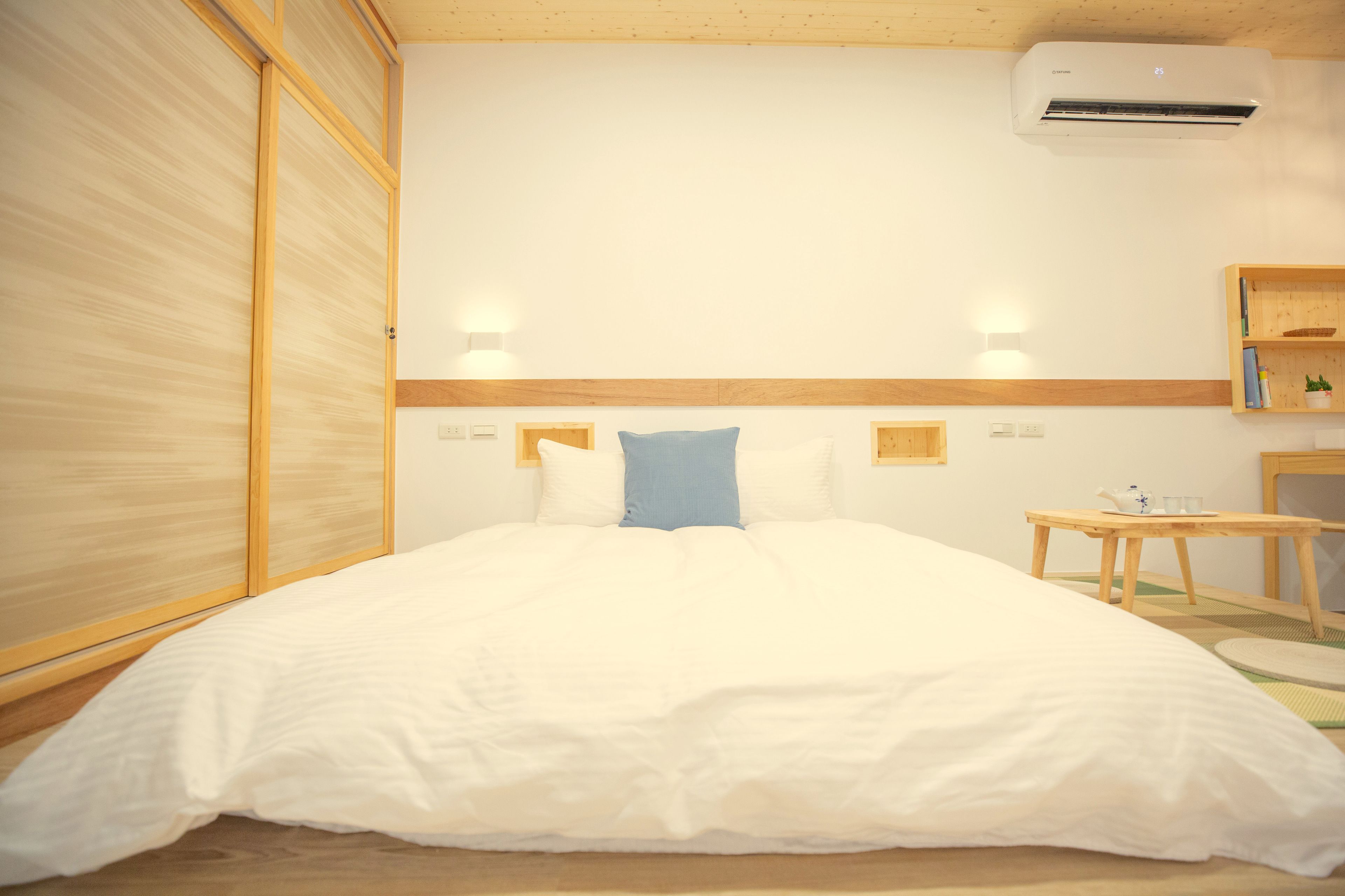 Una habitación de hotel con una cama grande, cabecera de madera, mesitas de noche y un aire acondicionado.