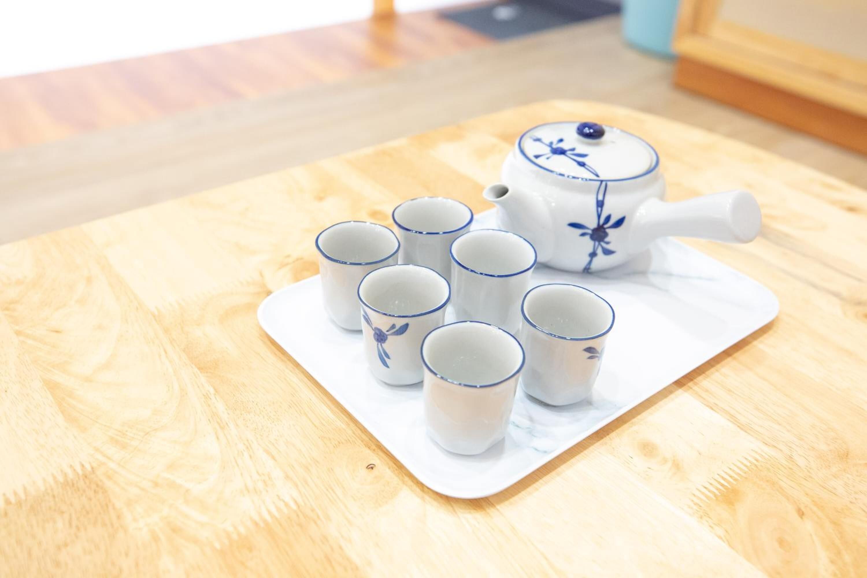 A white teapot with blue floral designs and six matching cups on a wooden table.