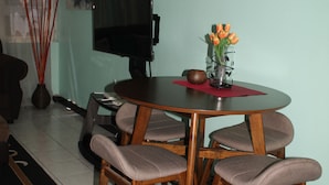 A dining area with a round table, six chairs, a TV, and a vase with flowers. - New Kingston Serenity at The Oxford (Kingston)