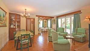 A dining area with a table and chairs, a chandelier, and a view through large windows. - Rustic - Cozy country house with pool in Mancor de la Vall, Mallorca (Inca)