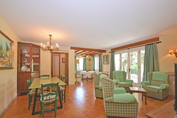 Un espace repas comprenant une table et des chaises, un lustre et une vue dégagée sur l’extérieur grâce à de grandes fenêtres.