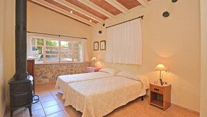A bedroom with two beds, a stone wall, a window, and a wood-burning stove. - Rustic - Cozy country house with pool in Mancor de la Vall, Mallorca (Inca)