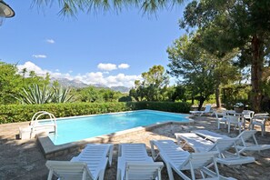 Une piscine bordée de chaises longues blanches et d’une bordure en pierre.