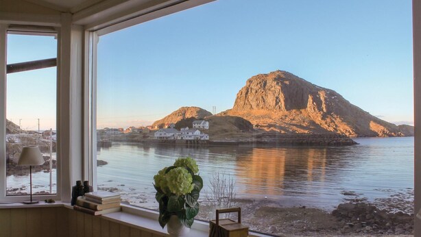 Ein Zimmer mit großem Fenster mit Blick auf ruhiges Gewässer und einen felsigen Hügel.