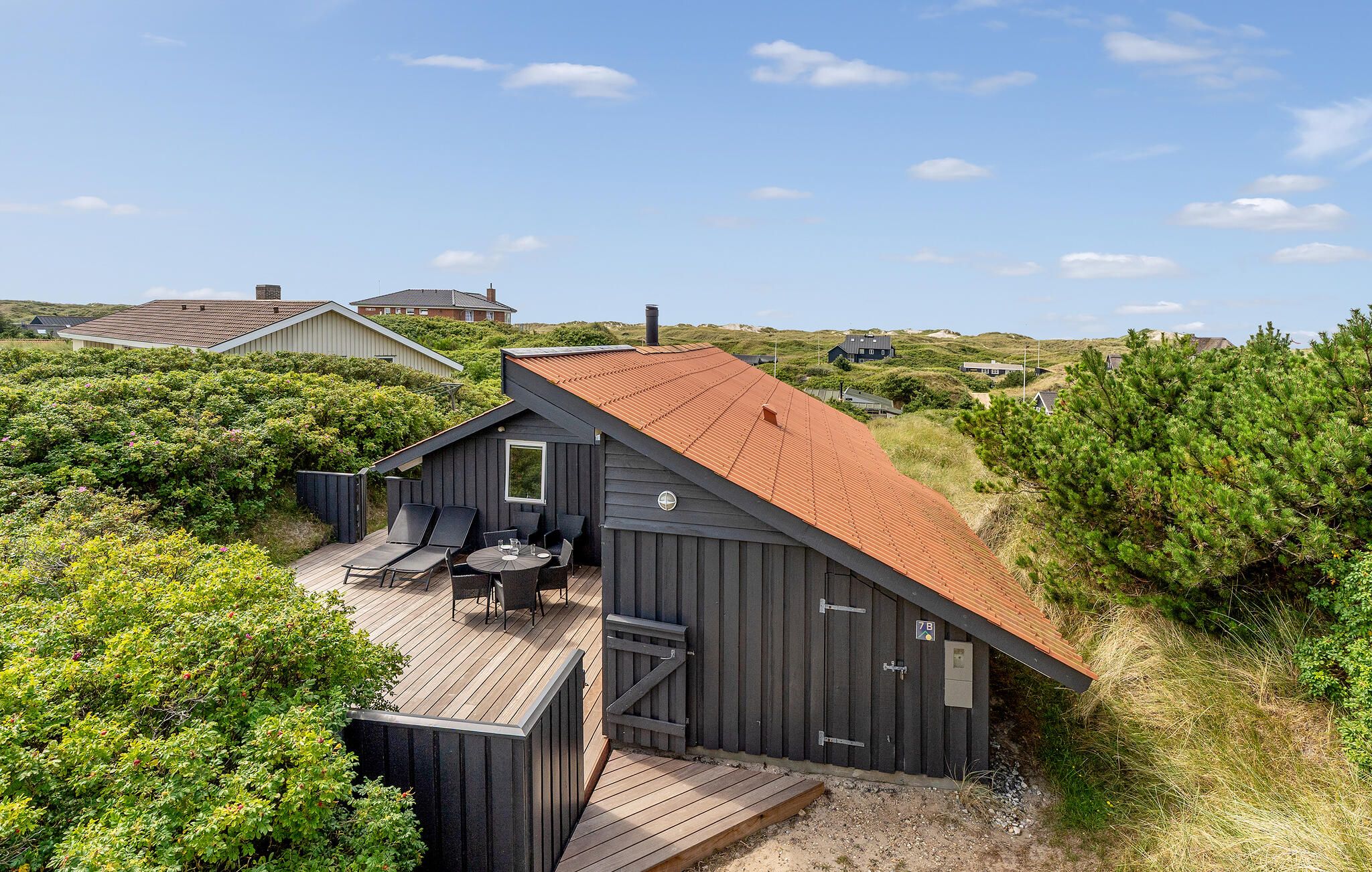 Ein modernes Strandhaus mit geneigtem Dach, einer Terrasse mit Sitzgelegenheit und Blick auf die umliegende Landschaft.
