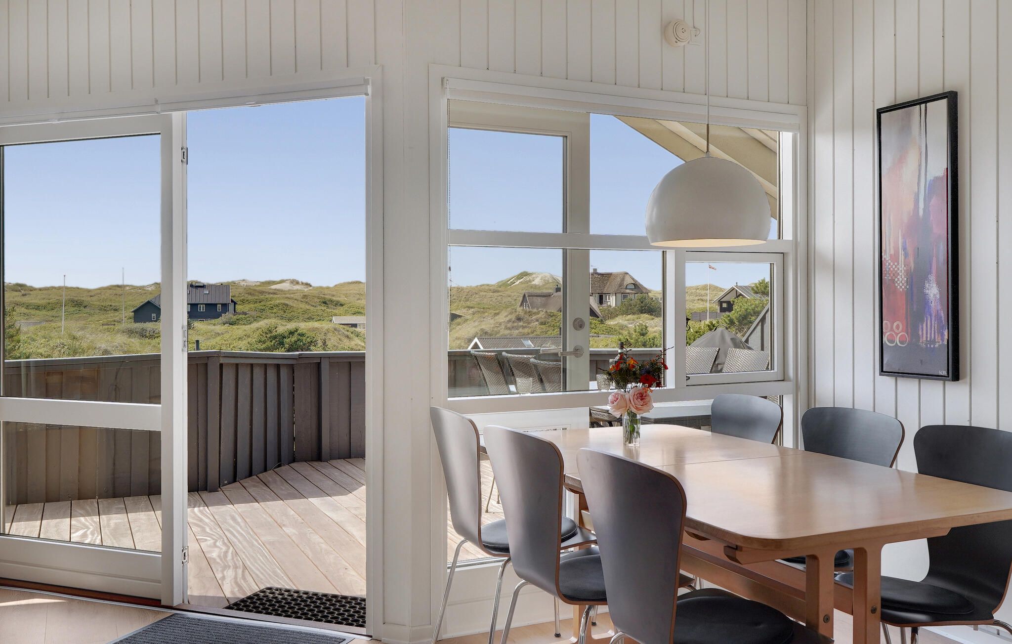 A room with a wooden table and chairs, large windows, and a view of the landscape.