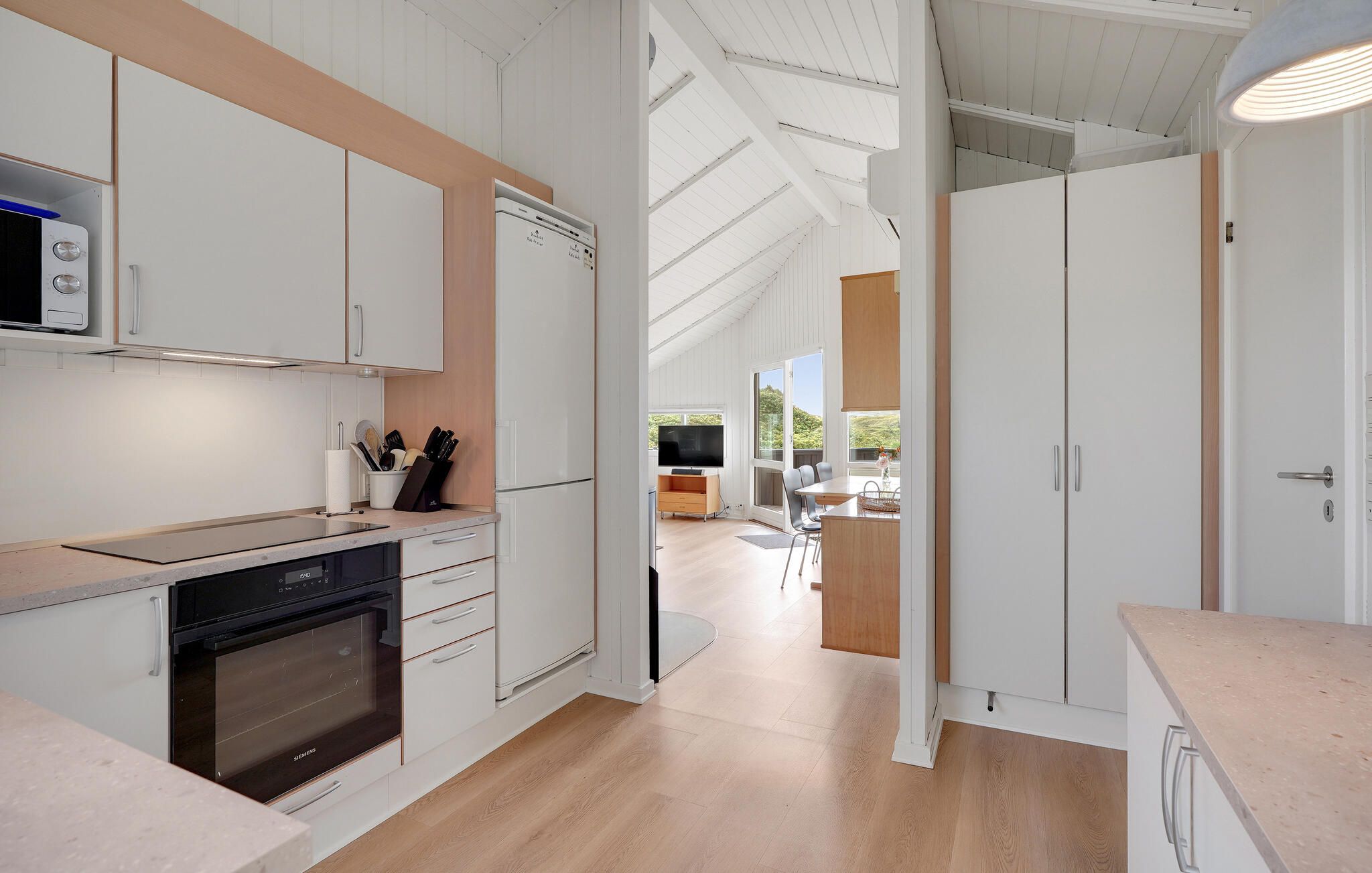 Een moderne keuken met witte kasten, een inbouwoven en een eethoek met een tafel en stoelen.