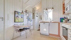 Une cuisine avec des armoires blanches, un lave-vaisselle, un four à micro-ondes et un évier. Une fenêtre laisse entrer la lumière naturelle et il y a une chaise à la table à manger.