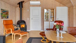 A cozy room with a wood-burning stove, leather chairs, a dining table, and a cabinet with glass doors. - Nice home in Ebeltoft with kitchen (Ebeltoft)