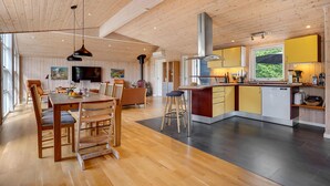 A modern kitchen with wooden cabinets, a central island, and a dining area with a wooden table and chairs. - Nice home in Ebeltoft with kitchen (Ebeltoft)