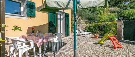 A patio with a table set for two, outdoor chairs, and a children's play area with a slide.