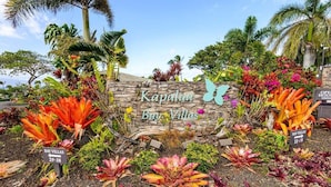 A sign for "Kapalua Bay Villas" with a stone wall and tropical plants. - Upgraded 1BD OceanFront Villa w AC Pool - Kapalua Bay Villa 23B1 (Lahaina)